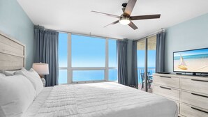 Een slaapkamer met een groot bed, een plafondventilator, een televisie en uitzicht op de oceaan.