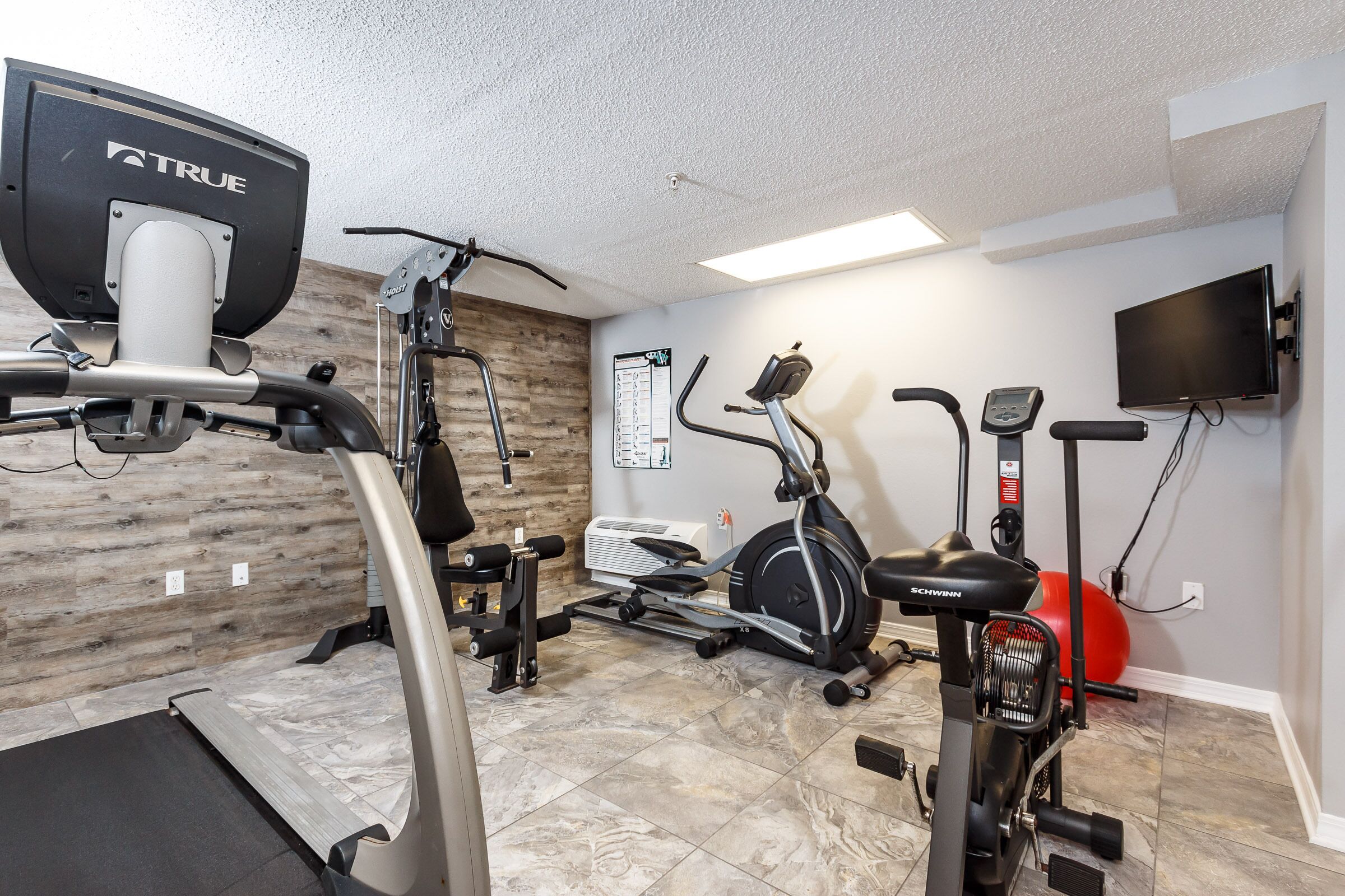 A home gym with various exercise equipment including a treadmill, stationary bike, and elliptical machine.
