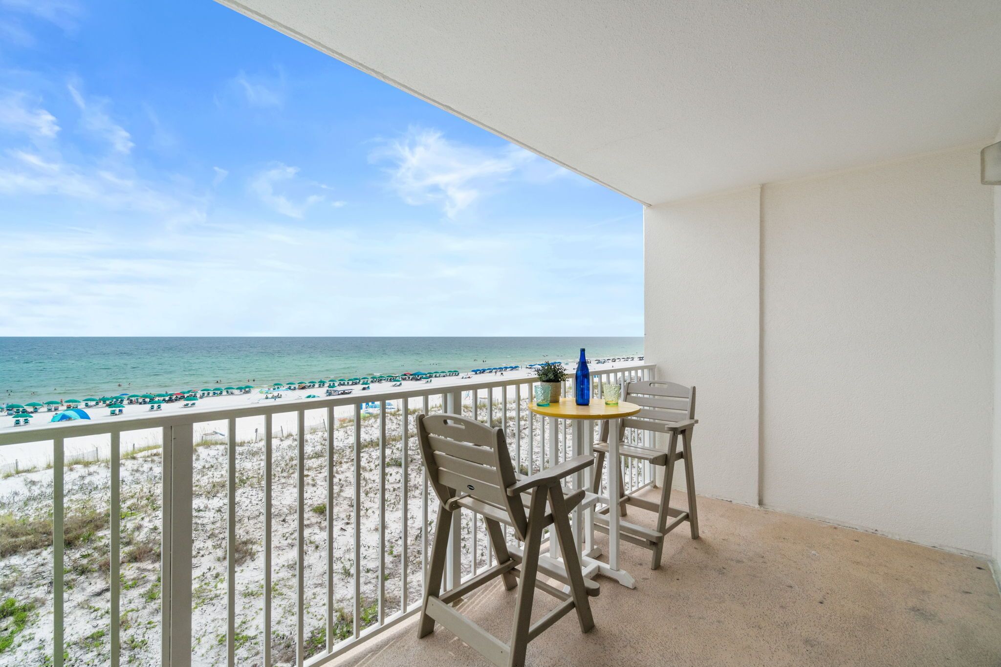 A balcony with a view of the beach, featuring two chairs and a small table with a bottle.