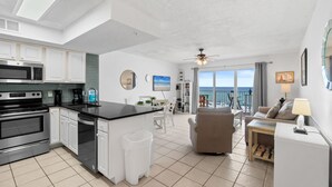 A modern kitchen with a central island, white cabinetry, and a dining area with a view of the ocean. - GD 406: Beachy Keen - Shell Yeah, It’s Beachfront! (Fort Walton Beach)
