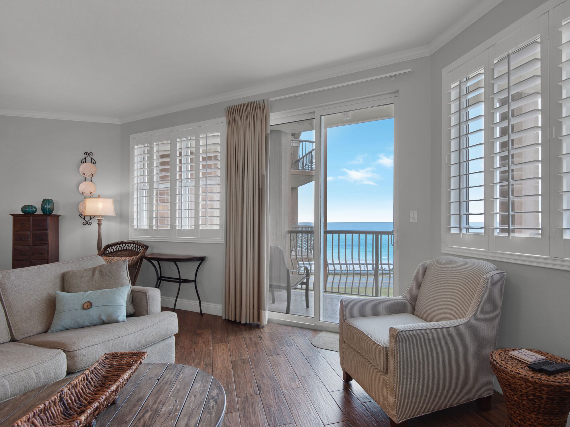 A living room with a sofa, armchair, and a small table. There is a view of the ocean through large windows.