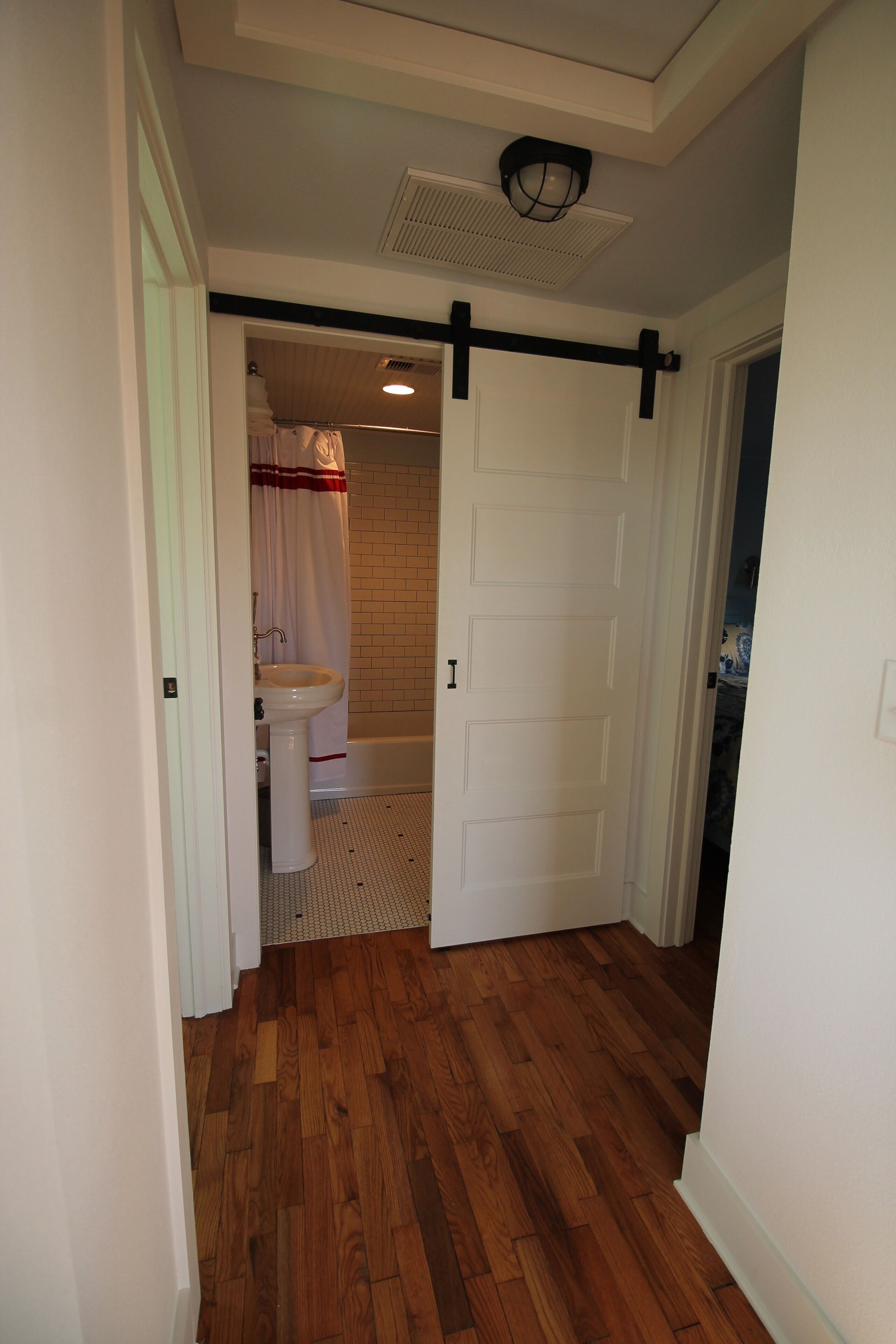 A hallway with wooden flooring, a white door, and a bathroom visible through an open door.