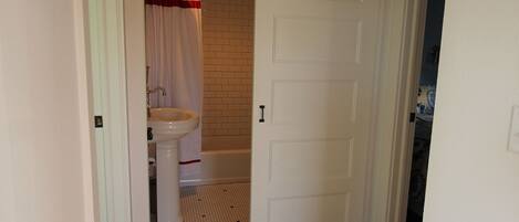A hallway with wooden flooring, a white door, and a bathroom visible through an open door.