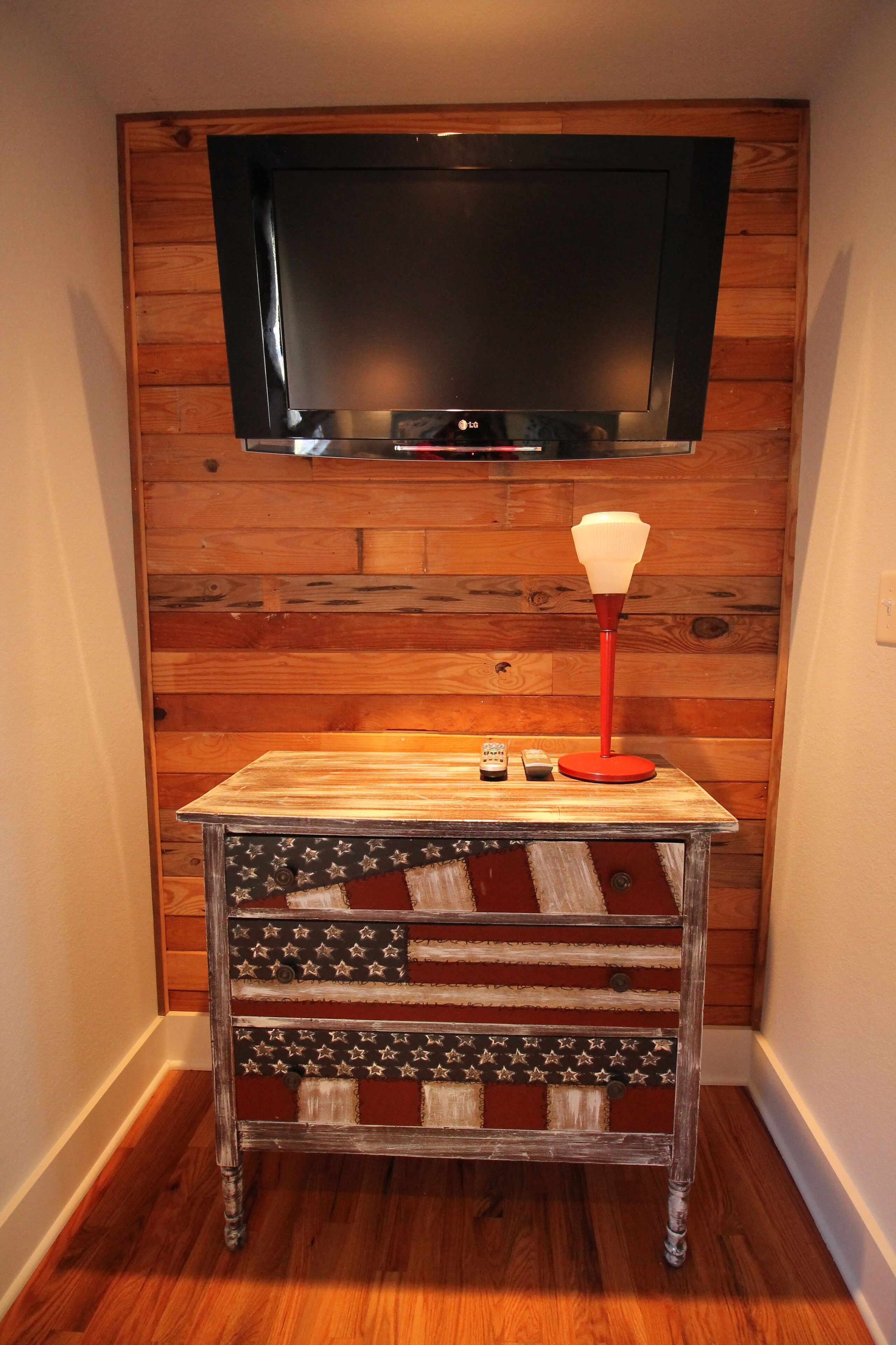 A wooden wall with a flat-screen TV mounted above a small table with a red lamp.