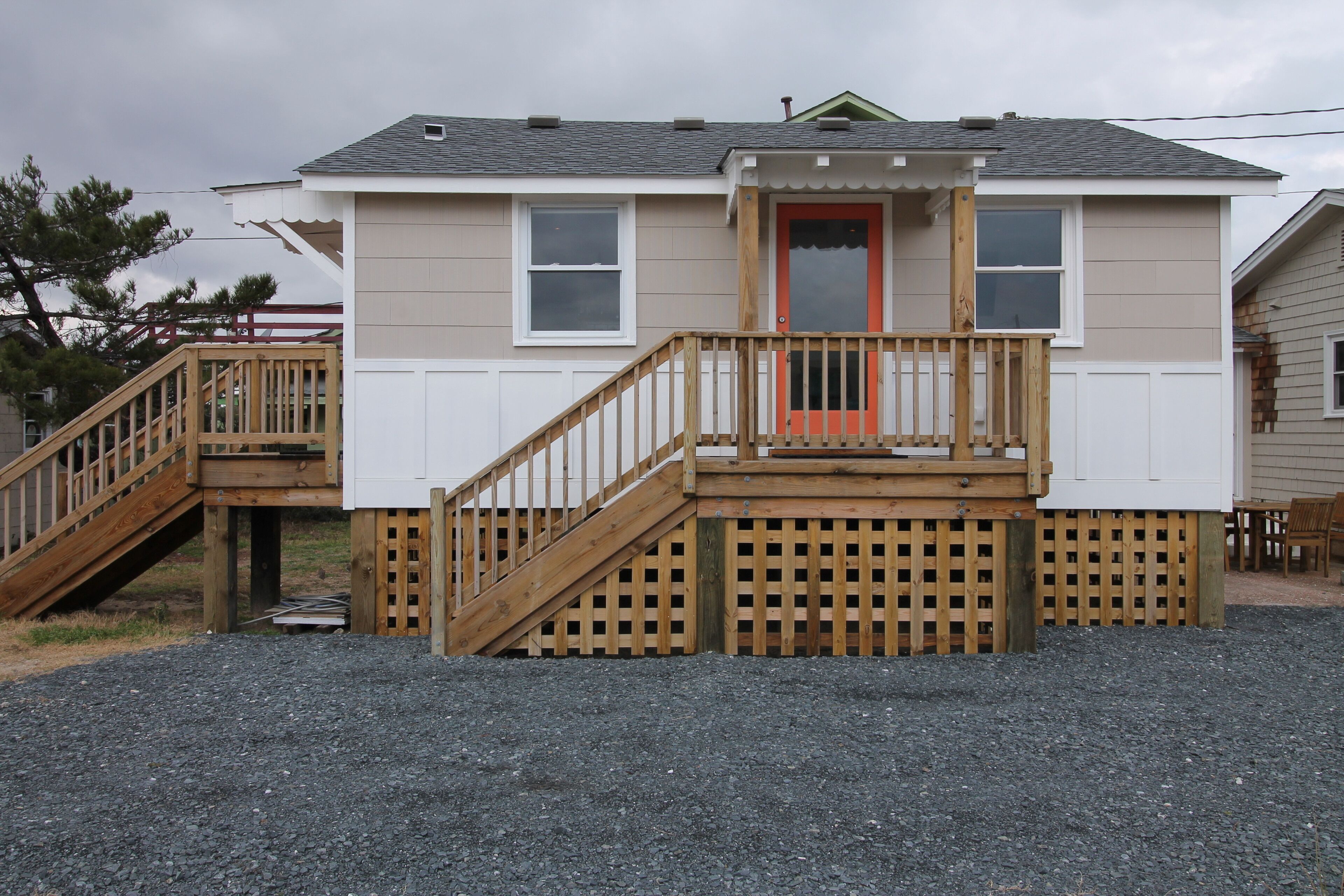 A two-story house with a wooden deck, a red door, and a staircase leading to the deck.