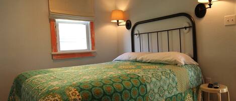A bedroom with a bed, a window, a wall-mounted lamp, and a wooden floor.