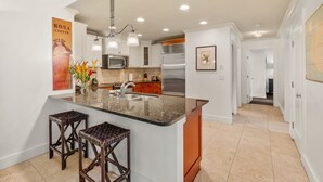 A modern kitchen with a large island, stainless steel appliances, and a hanging light fixture. - Luxury Poipu 4br Villa with AC Walk to the Beach! (224) (Koloa)