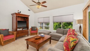 A spacious living room with a wooden coffee table, a grey sofa, a wicker armchair, and a television on a wooden cabinet. - Luxury Poipu 4br Villa with AC Walk to the Beach! (224) (Koloa)