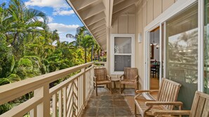 A balcony with wooden furniture, a view of tropical foliage, and a building entrance. - Luxury Poipu 4br Villa with AC Walk to the Beach! (224) (Koloa)