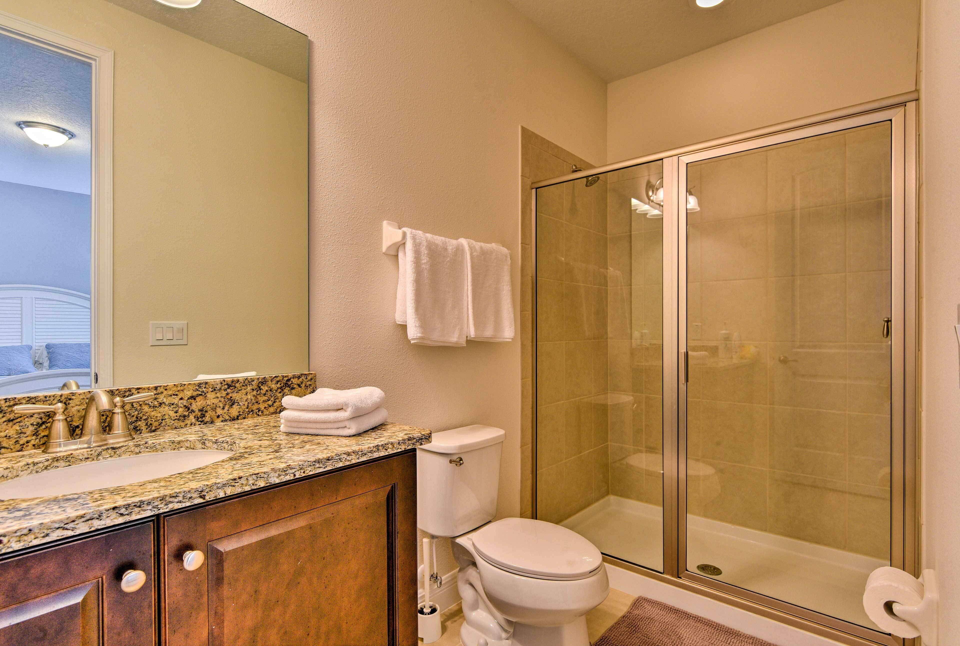A bathroom with a granite countertop, a toilet, a glass shower enclosure, and a large mirror.
