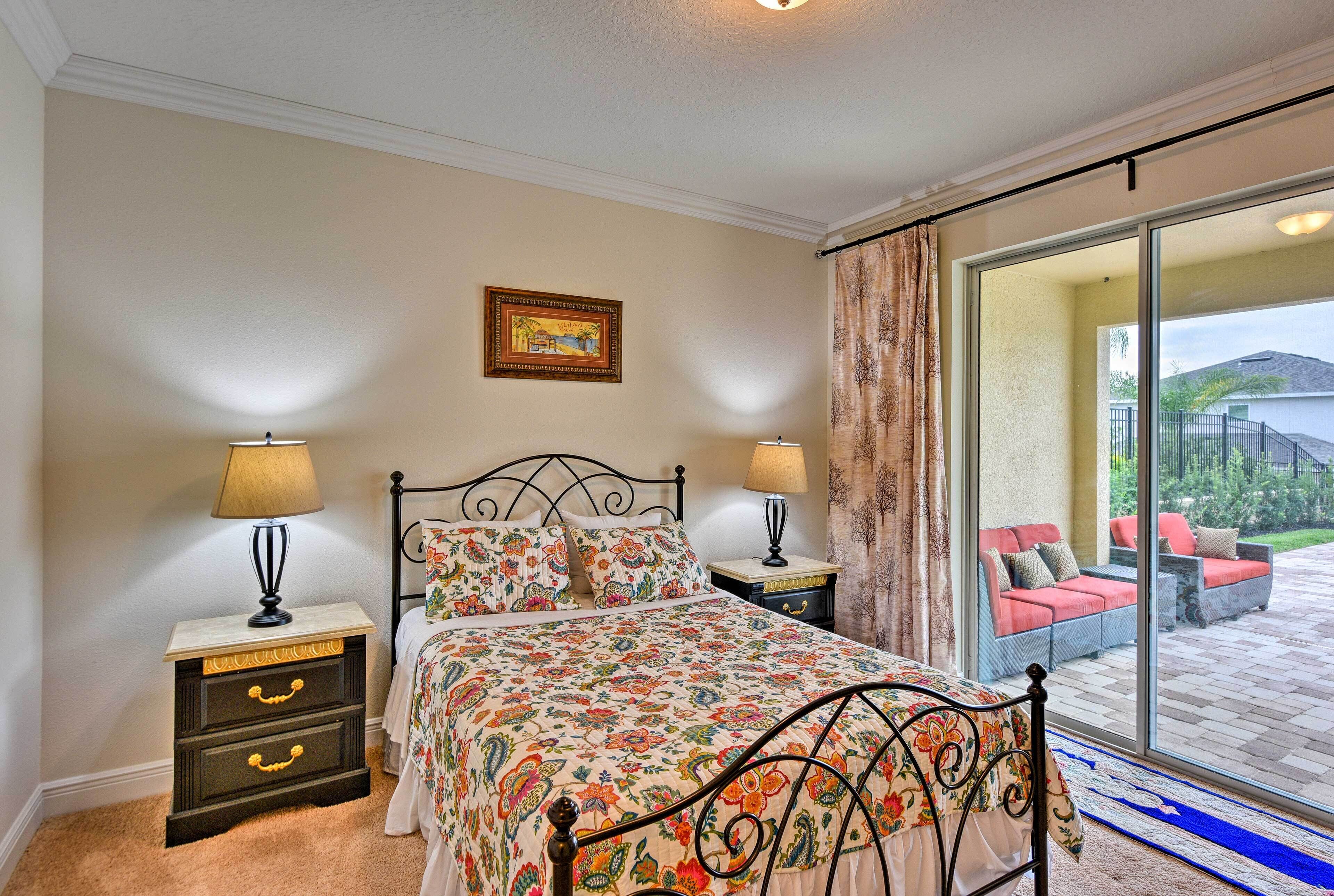 Une chambre à coucher comprenant un lit, deux tables de chevet avec des lampes, une commode avec des tiroirs, une grande fenêtre avec des rideaux et une vue sur un espace extérieur aménagé pour se détendre.
