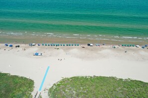 Ein Strand mit Reihen von Sonnenschirmen und Liegestühlen, ein sandiger Uferstreifen und ein freier Blick auf den Ozean.