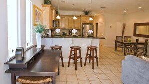 A modern kitchen with wooden cabinets, a stainless steel refrigerator, and a bar area with stools.