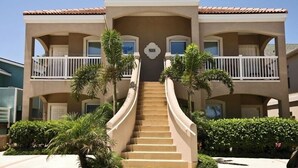 A multi-story hotel with a central staircase, balconies, and palm trees.