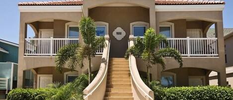 Un hotel de varios pisos con una escalera central, balcones y palmeras.
