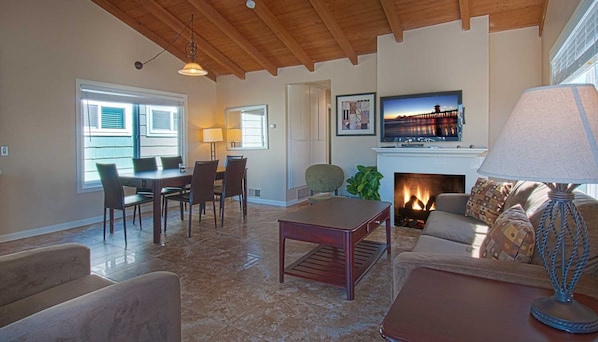 A living room with a fireplace, a television mounted above it, and a dining area with a table and chairs.