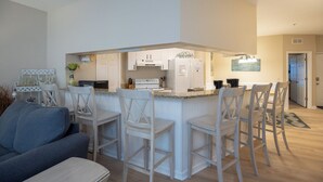 Une cuisine compacte avec des meubles blancs, un îlot central doté de tabourets de bar et un coin repas avec un canapé bleu.