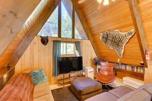 Un interior acogedor de madera, con un televisor grande, estanterías y una obra de arte original en la pared.