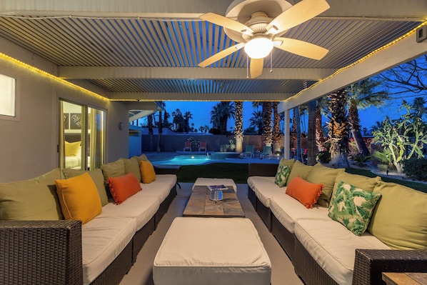 An outdoor seating area with wicker furniture, a ceiling fan, and a view of a pool and garden.