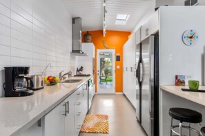 Eine moderne Küche mit weißen Schränken, einem Edelstahl-Kühlschrank, einer Kaffeemaschine und einer Obstschale.
