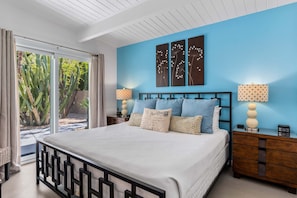 Ein Schlafzimmer mit Bett, Nachttischen, einer blauen Wand und Blick auf einen Garten.