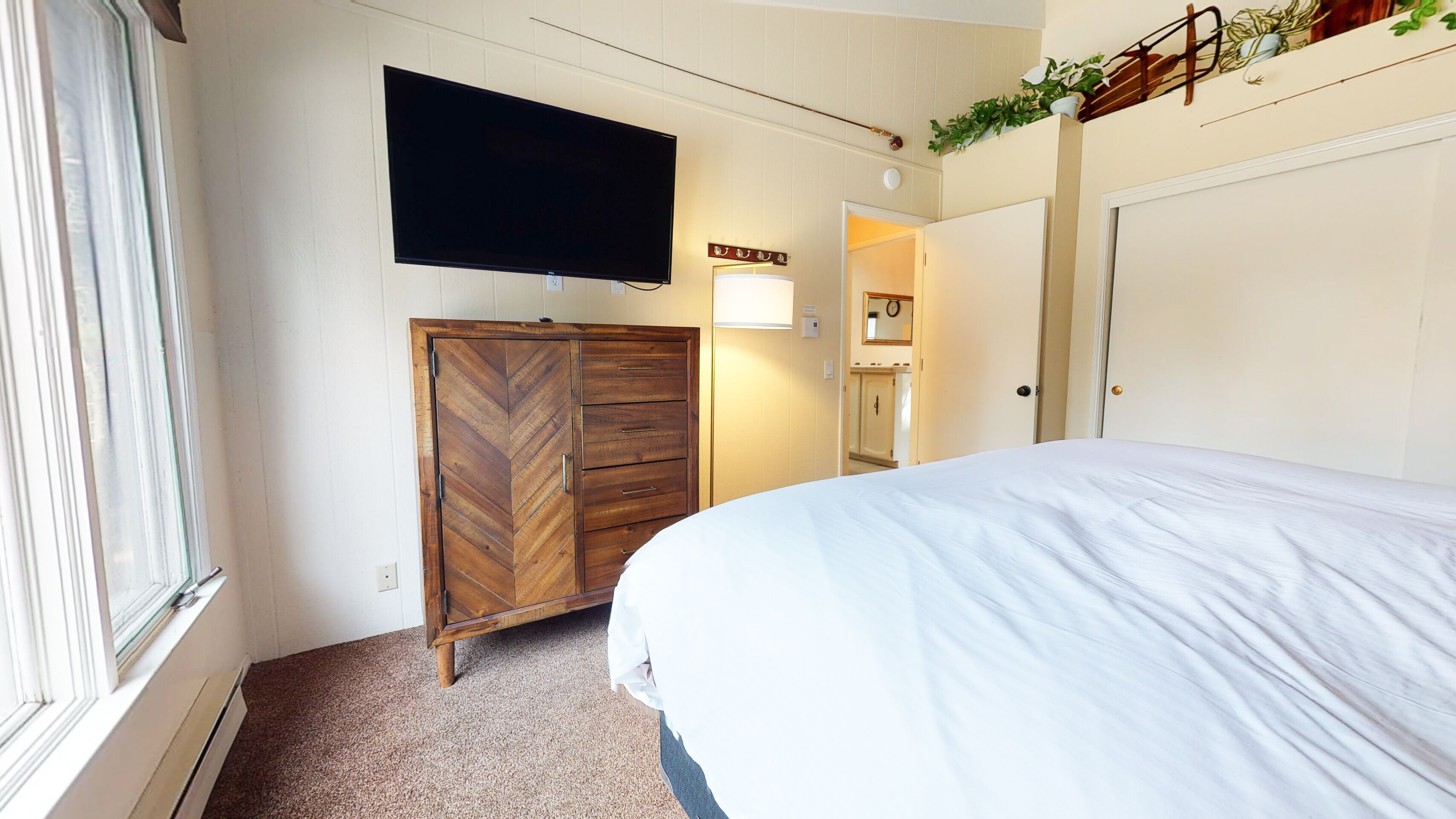 Ein Schlafzimmer mit Bett, einem an der Wand befestigten Fernseher, einem Holzschrank und einer Tür zu einem Badezimmer.