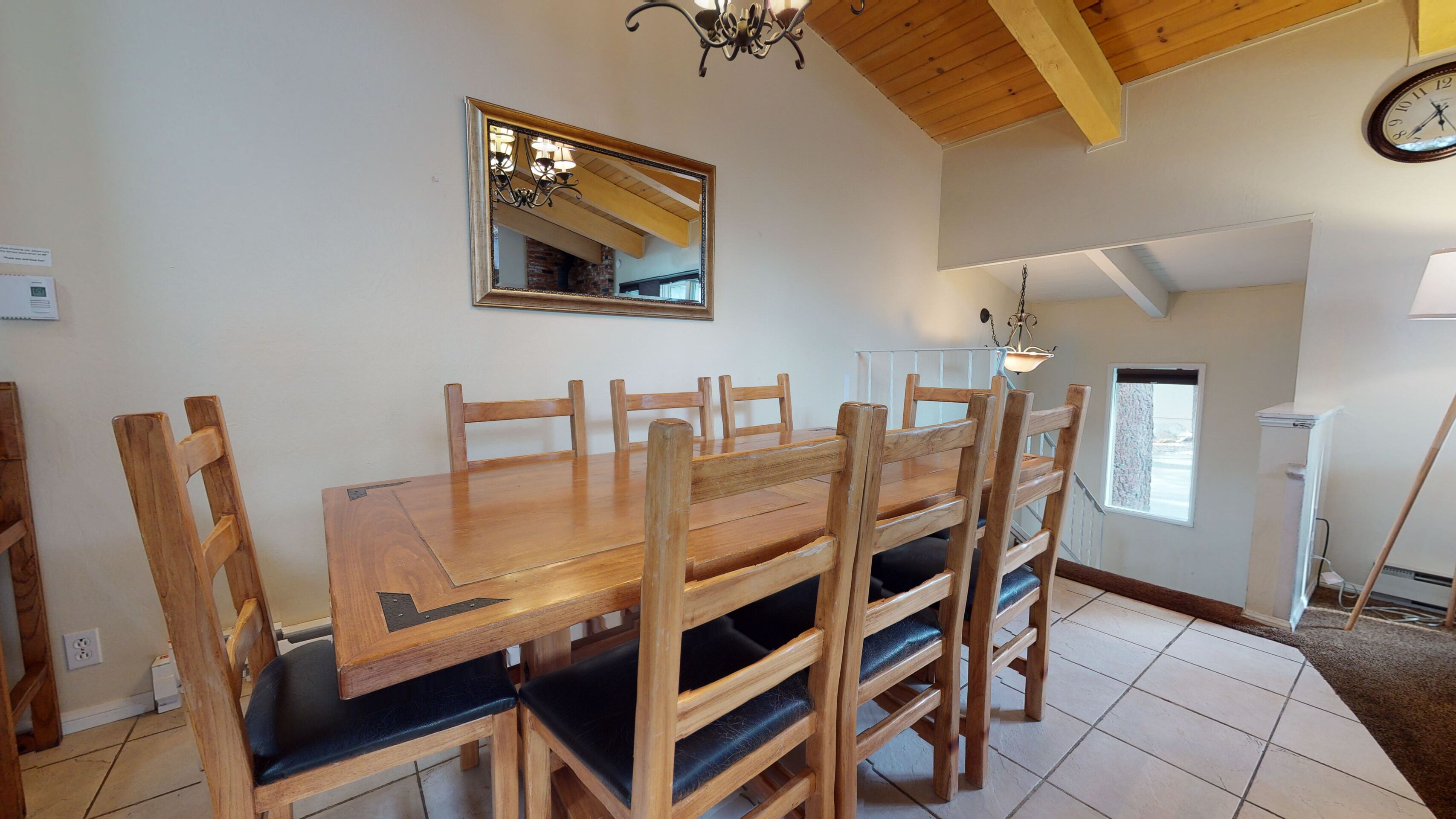 A dining area with a wooden table and chairs, a mirror on the wall, and a chandelier.