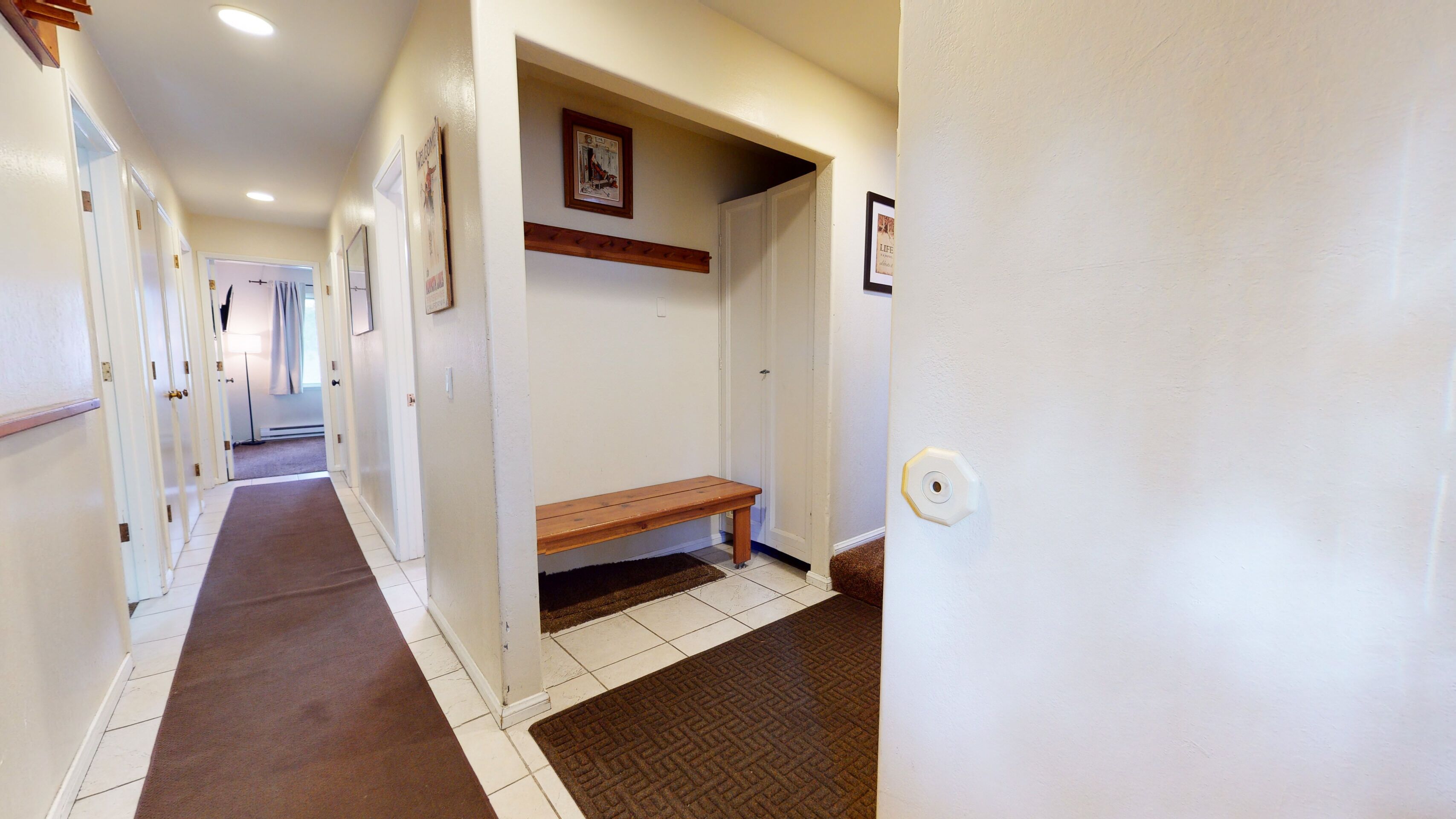 A hallway with a bench, white walls, and a door with a picture frame.