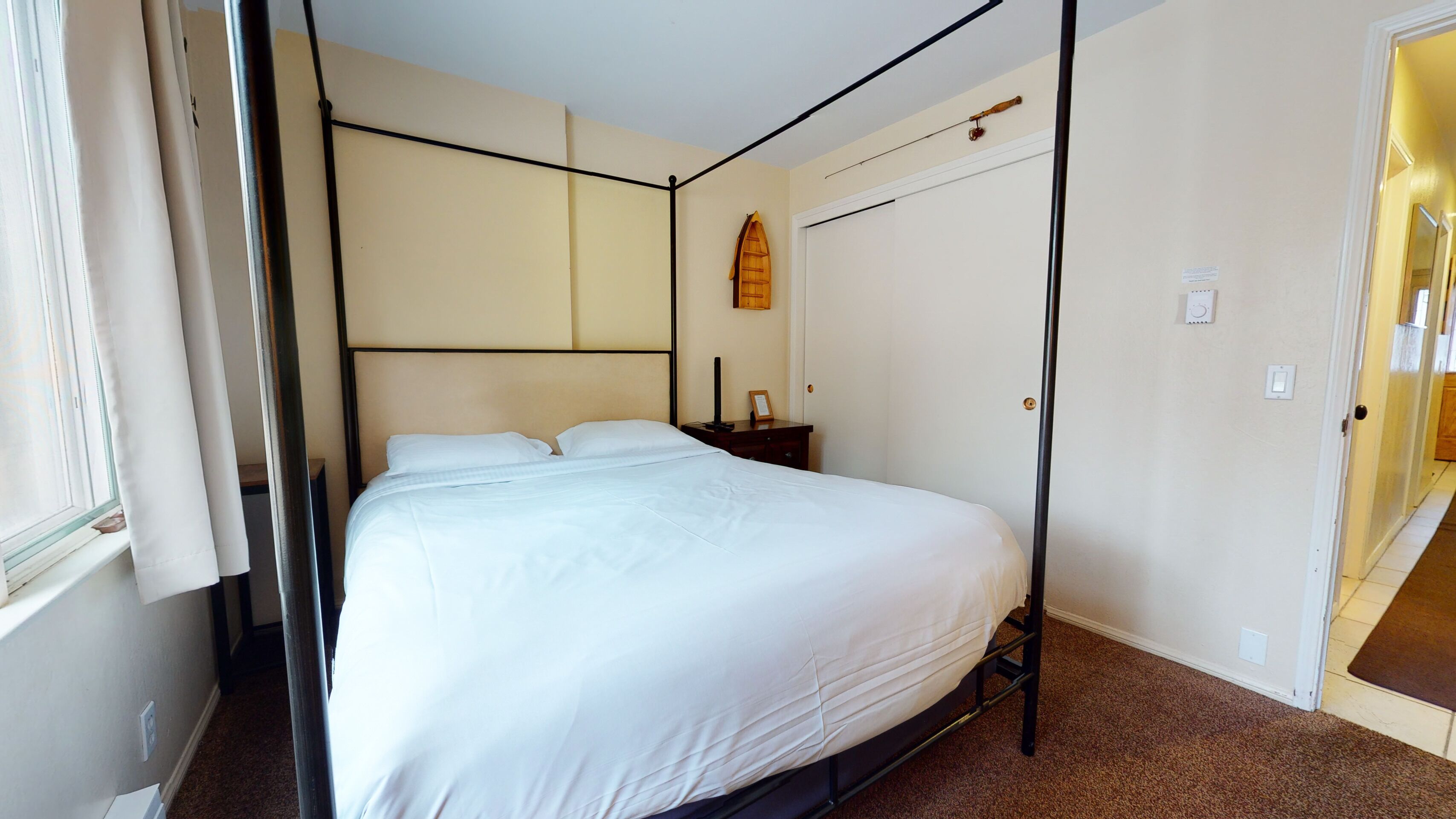 A single bed with a metal frame, a bedside table, a wall-mounted clock, and a door to the right.