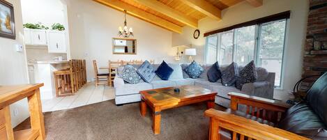 A cozy living room with a grey sofa, wooden coffee table, and a dining area with wooden chairs and a small table.