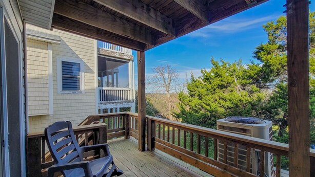 A covered porch with a wooden railing, a single black chair, and an air conditioning unit. - Stay Coastal at Fenway at the Beach (North Topsail Beach)