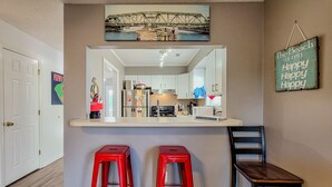 A kitchen with a white countertop, red stools, and a hanging sign that says "The Beach is my Happy Happy Happy." - Stay Coastal at Fenway at the Beach (North Topsail Beach)