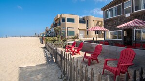 Een vakantiehuis aan het strand met rode Adirondack-stoelen, een houten omheining en een gebouw met een bord waarop zomer en winter staan.