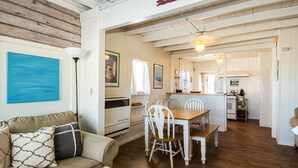 Een gezellige woonkamer met een houten vloer, een eettafel met witte stoelen en een keuken met witte kastjes en een fornuis.