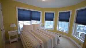 Un dormitorio con cama, mesita de noche y dos ventanas con persianas.
