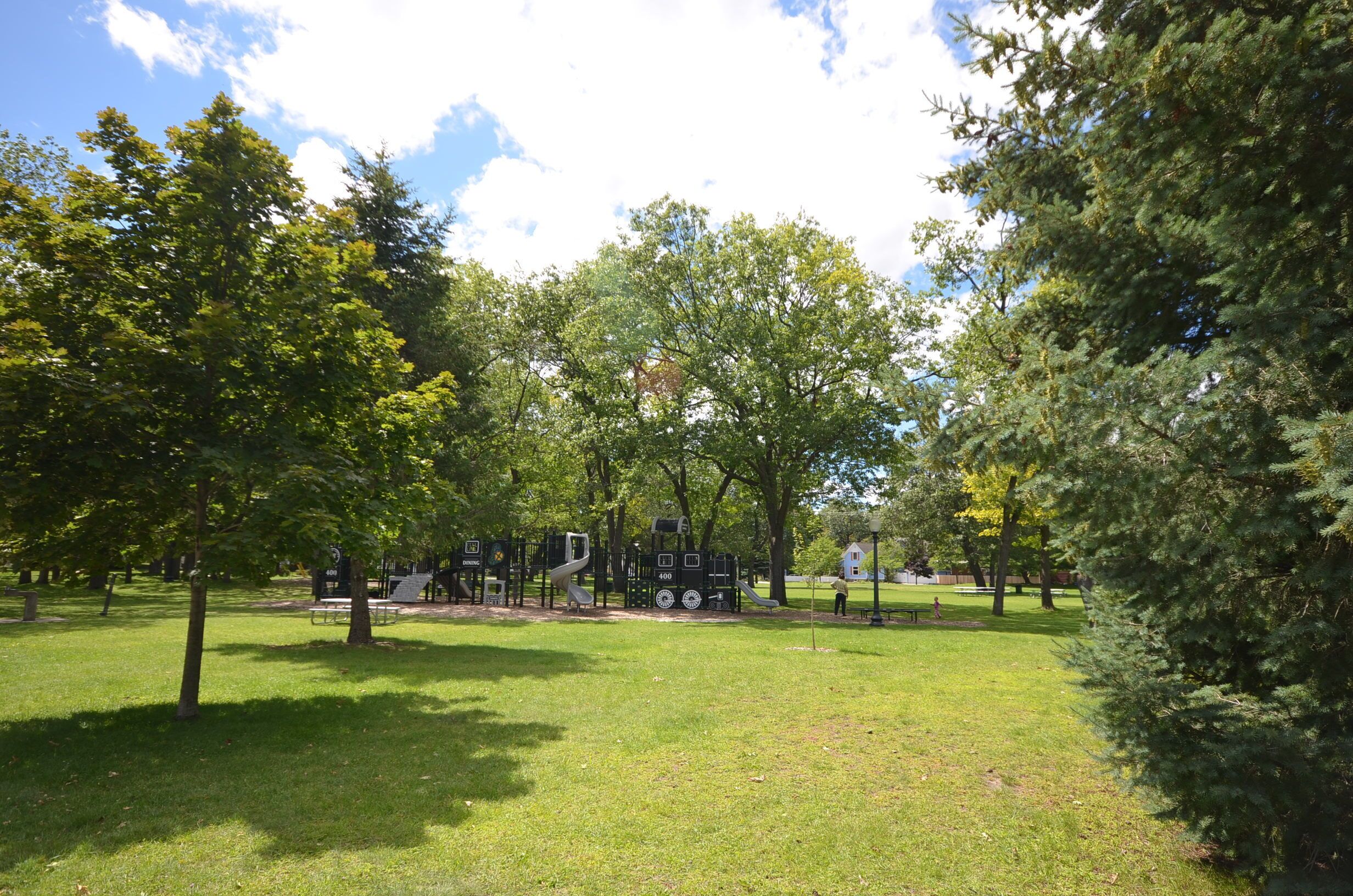A park with playground equipment, benches, and trees.