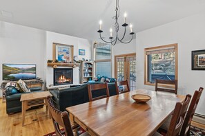 A cozy living room with a fireplace, a dining table, and a large window. - Ski-in/ski-out, Private Garage Parking! (Breckenridge)