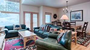 A cozy living room with a large window, a fireplace, and a dining area with a table and chairs.