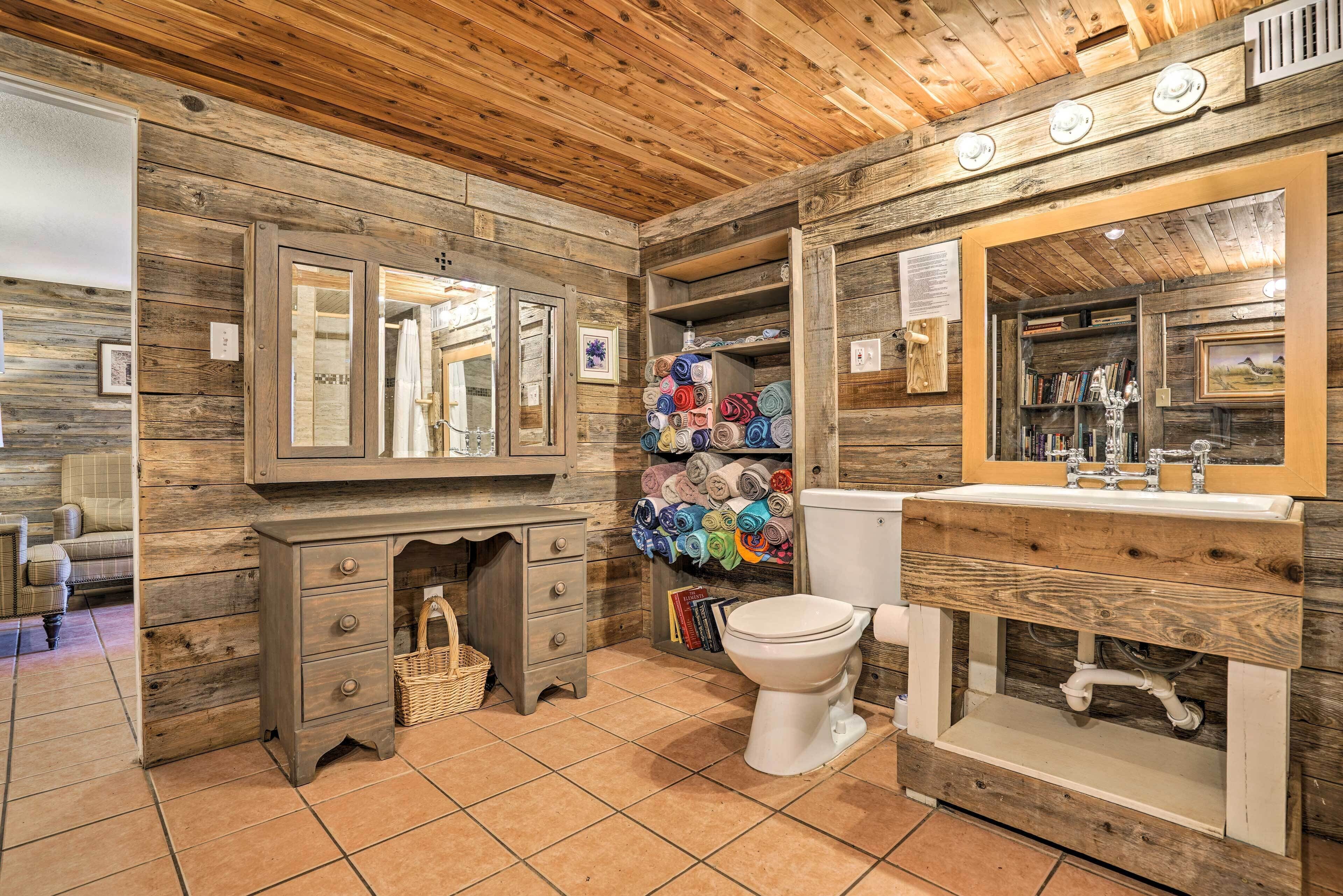 Ein rustikales Badezimmer mit Holzwänden, einem Holzwaschtisch, einer Toilette und einem Regal mit zusammengerollten Handtüchern.