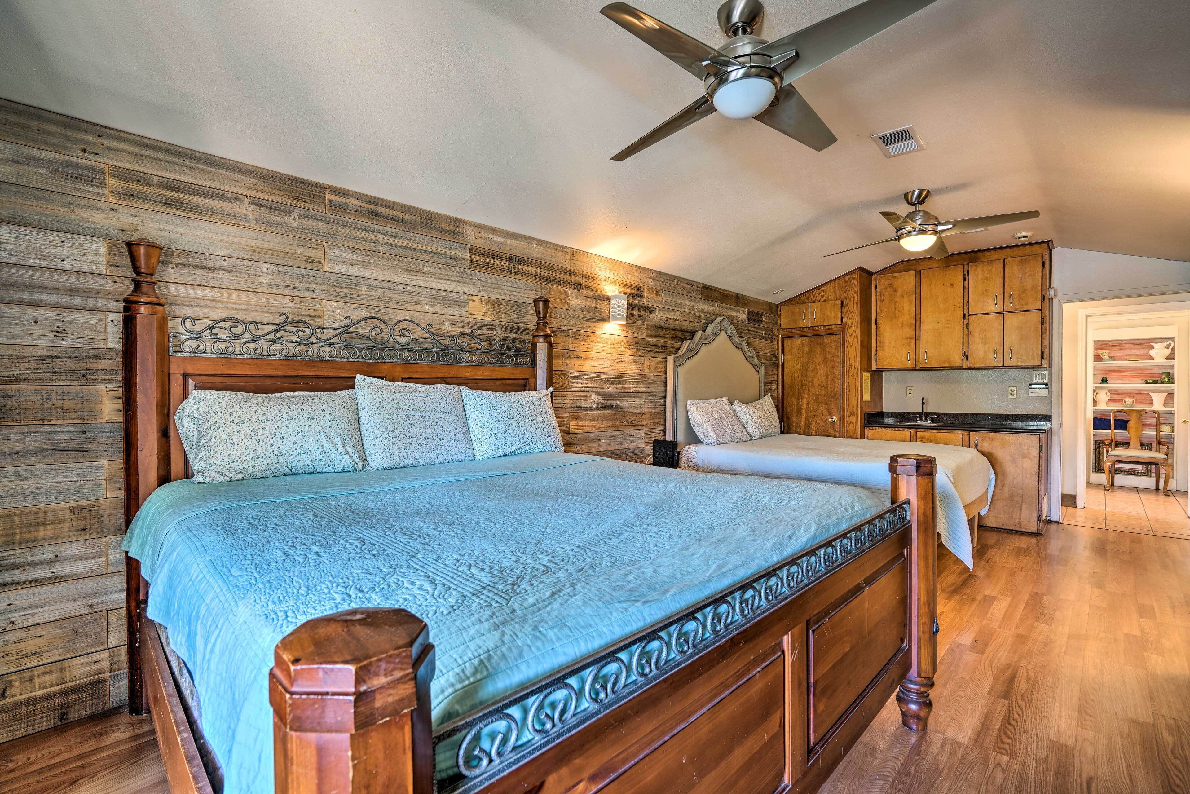 Un dormitorio con cabecera de madera, cama con colcha azul, ventilador de techo y armarios de madera en la habitación contigua.