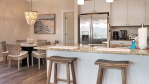 Una cucina moderna con isola centrale, mobili bianchi, elettrodomestici in acciaio inossidabile e un'area pranzo con sedie in vimini.