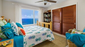 Ein Schlafzimmer mit einem Bett, einem Holzstuhl, einem Bücherregal und Blick aufs Meer.