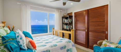 A bedroom with a bed, a wooden chair, a bookshelf, and a view of the ocean.
