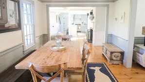A spacious dining area with a wooden table and chairs, a rug, and a view into the kitchen. - School Street in the Old Village!! Charming, new construction with attention to detail! (Chatham)