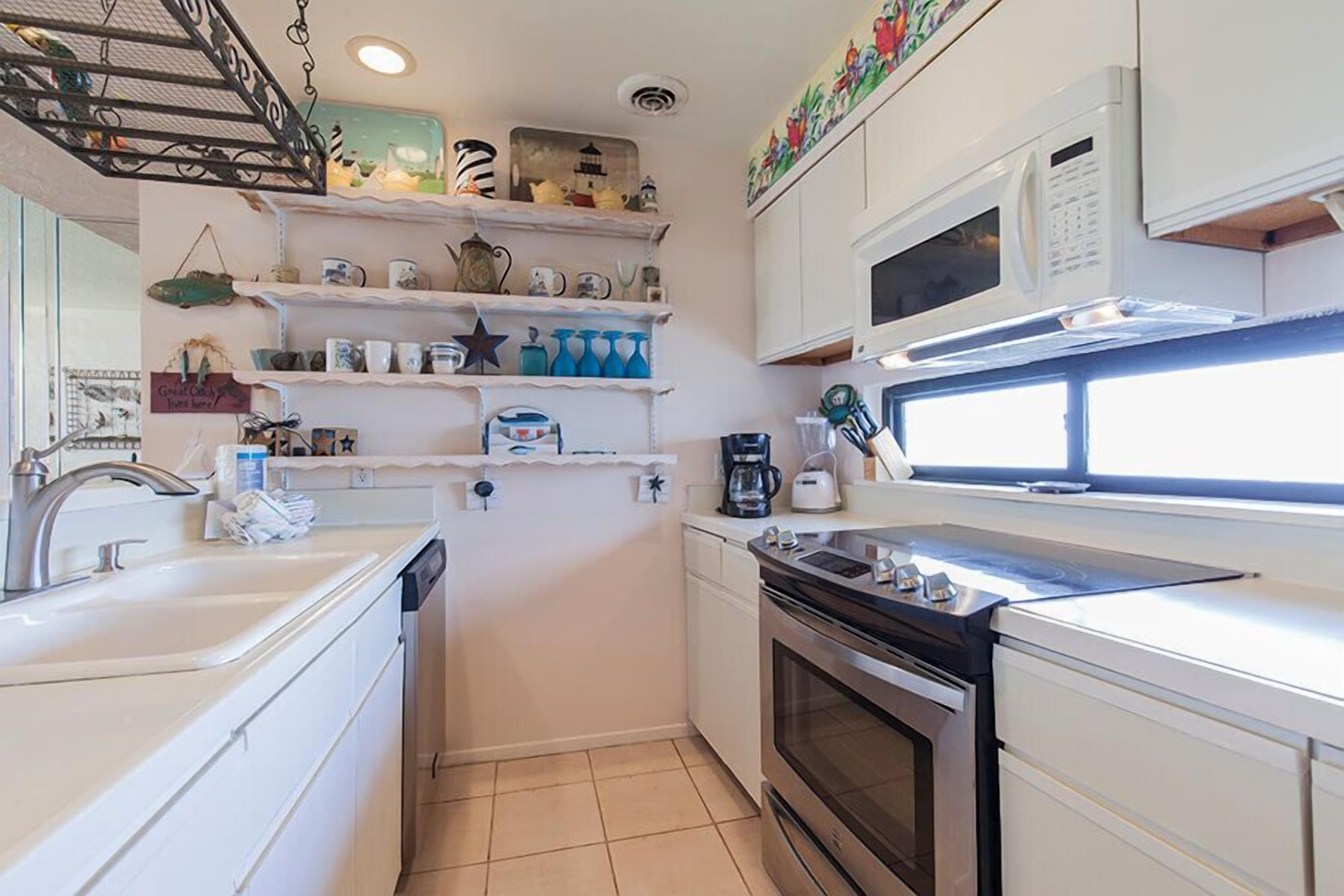 A compact kitchen with white cabinets, a microwave, a stove, and shelves with various kitchen items.