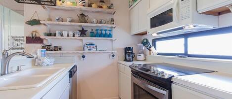 A compact kitchen with white cabinets, a microwave, a stove, and shelves with various kitchen items.