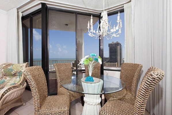 A balcony with wicker furniture, a glass table, and a chandelier.
