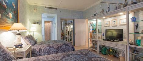 A hotel room with two beds, a television, a glass display cabinet with decorative items, and a painting of fish on the wall.