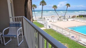A balcony with a view of the ocean and a pool area with lounge chairs and umbrellas.