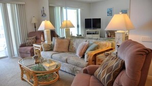 A living room with a sofa, armchairs, a glass coffee table, and a television.